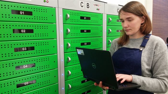 A student looks at a laptop while standing in front of the green laptop loan lockers in the Doug Ellis Suite at the Medical School.
