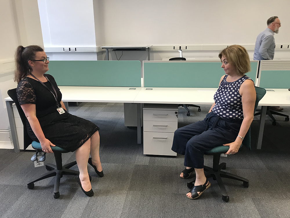 Two members of staff sitting in new office chairs