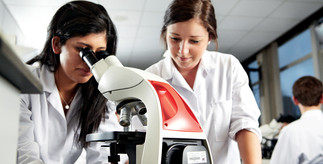 two women undertaking scientific research in a lab with one looking down a microscope