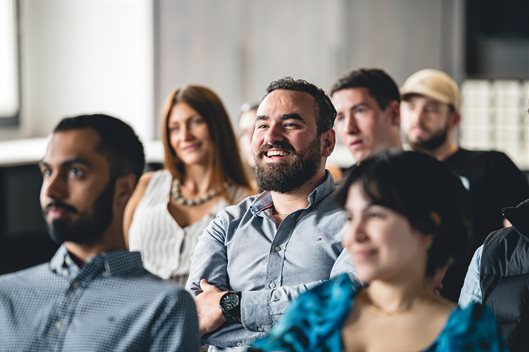 pERSON SMILING WHILST SITTING IN AN AUDIENCE AT A PRESENTATION