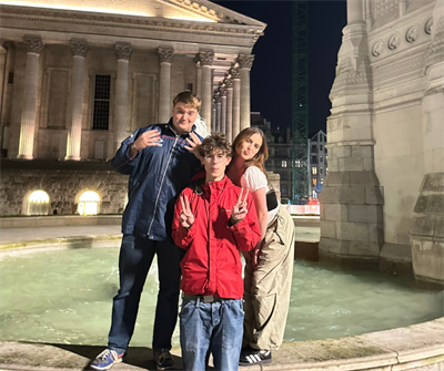 2 male students and a female student stand on the edge of a fountain, posing to the camera
