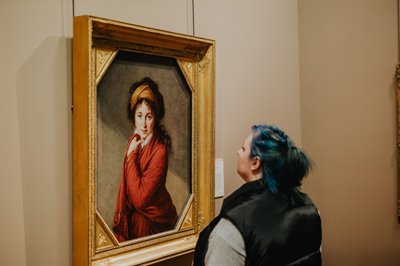Female student is looking at a painting of a woman in a red dress