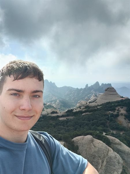Student Dan smiles on top of a mountain.