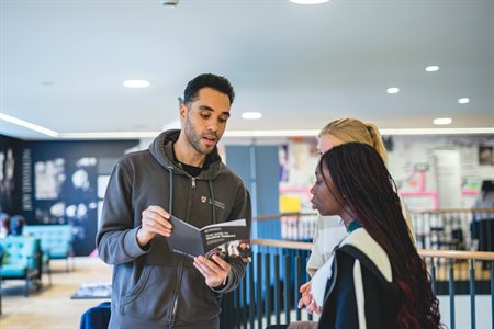 A staff member shows two students the Student Support Guide.