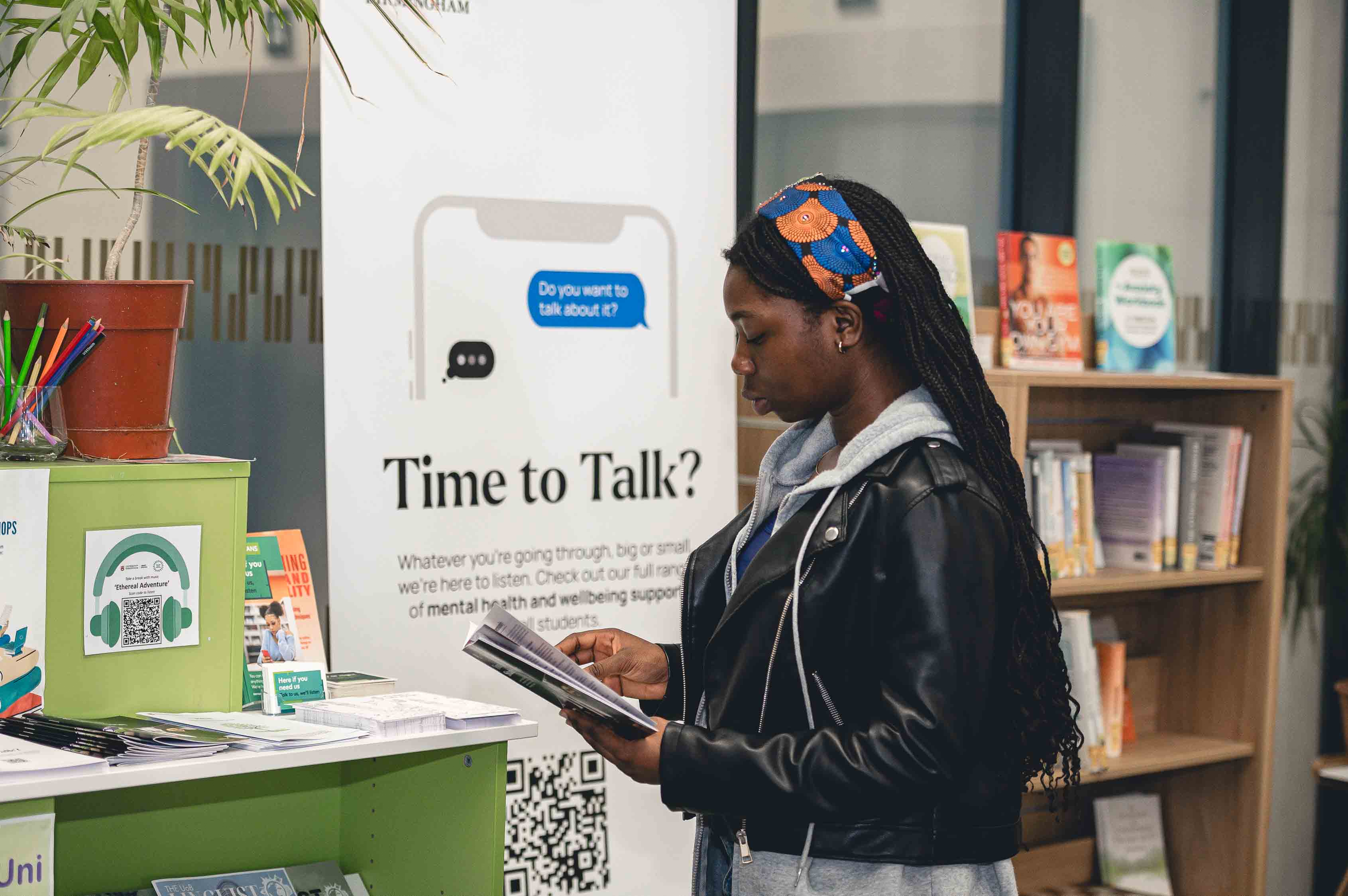 Female student stands in a library reading a booklet